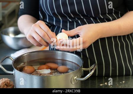 Una chef donna si vede sbucciare uova sode in cucina. Foto Stock