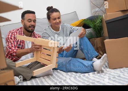 Una coppia, circondata da scatole mobili, assembla uno scaffale fai-da-te, personalizzando il loro nuovo spazio abitativo Foto Stock
