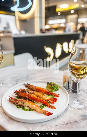 Langoustine con salsa di spinaci su un piatto bianco su un tavolo di marmo con un bicchiere di vino bianco. Foto di alta qualità Foto Stock