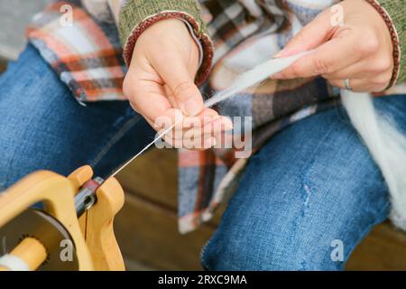 La donna sta girando lana su una ruota di legno che gira. Primo piano delle mani di una donna che lavora a maglia in lana Foto Stock