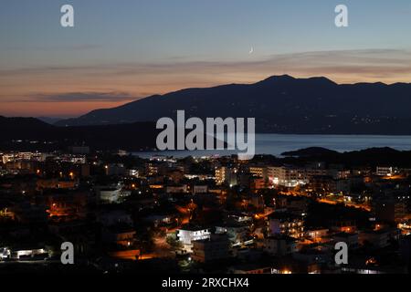 Vista notturna della città di Ksamil in Albania sullo sfondo dell'isola di Corfù e della luna. Splendida riviera albanese Foto Stock