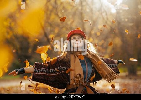 Ciao autunno. felice donna moderna di 40 anni con cappello rosso con sciarpa e guanti che gioisce nel parco cittadino. Foto Stock