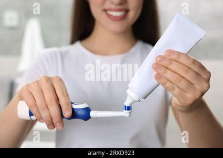 Donna che strizza dentifricio dal tubo allo spazzolino elettrico in bagno, primo piano Foto Stock