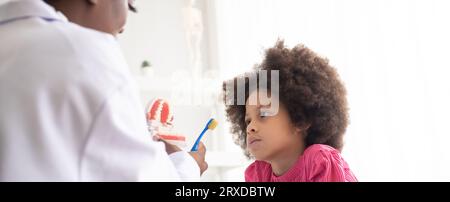 Dentista afroamericano che spiega ai bambini afro di razza mista come lavarsi i denti. Il concetto medico e sanitario per i bambini. Foto Stock