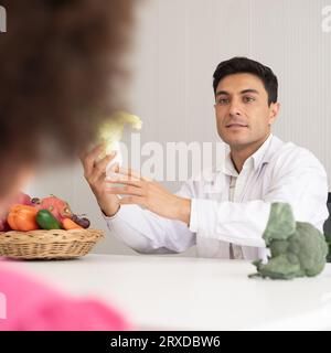 Medico nutrizionista ispanico che consulta un bambino di razza mista con la madre afroamericana su una nutrizione. Verdure cibo - un nuovo modo per il bene Foto Stock