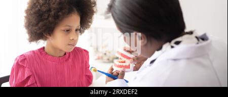 Dentista afroamericano che spiega ai bambini afro di razza mista come lavarsi i denti. Il concetto medico e sanitario per i bambini. Foto Stock