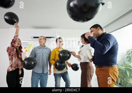 Manager e sviluppatori felici e gioiosi che lanciano palloncini e ballano Foto Stock