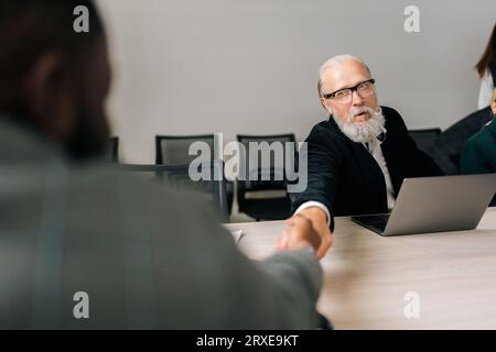 Vista posteriore delle strette di mano per l'irriconoscibile uomo d'affari africano e adulto adulto adulto adulto ceo maschio che è appena finito o affare di successo sul lavoro Foto Stock