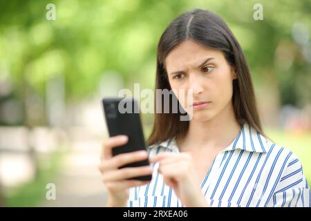 Donna che legge messaggi sospetti al telefono in un parco Foto Stock