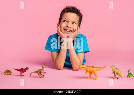 Foto di un simpatico e sognante bambino che indossa una maglietta blu che si gode dei giocattoli preferiti, spazio vuoto, sfondo di colore rosa isolato Foto Stock