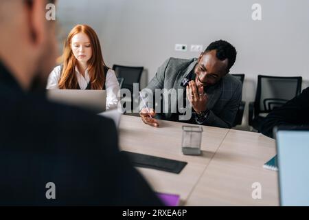 Retrospettiva del processo negoziale in sala riunioni tra partner commerciali positivi multietnici. Diversi uomini d'affari si riunirono in ufficio per parlare Foto Stock
