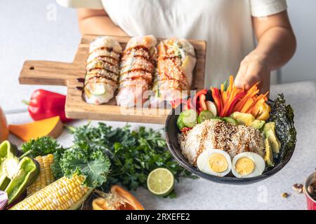 Recipiente con verdure, riso e involtini primavera in mani femminili in cucina. Foto Stock