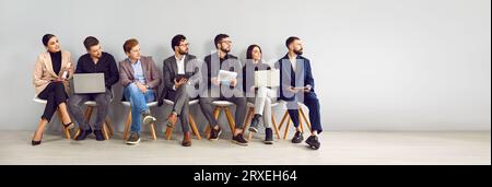 Uomini d'affari seduti in fila che guardano da parte Foto Stock