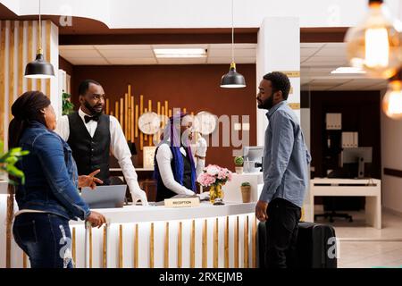 Gente stanca e infelice i turisti in piedi alla reception in attesa della procedura di check-in, si sentono stanchi e assonnati dopo un lungo volo. Una coppia afro-americana arriva al resort di lusso e aspetta che la camera sia pronta Foto Stock