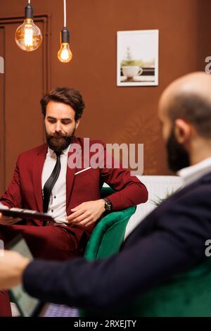 In attesa alla reception dell'hotel, gli uomini d'affari hanno usato il tempo per rivedere gli itinerari e i preparativi per le riunioni internazionali. I partner aziendali guardano gli appunti della conferenza nella hall. Foto Stock