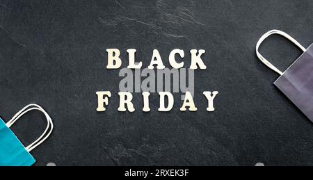 Testo in legno Black friday e sacchetti di carta su sfondo nero testurizzato, vista dall'alto. Foto Stock