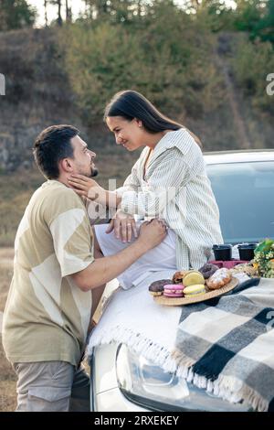 Una coppia felice trascorre un fine settimana estivo con un'auto fuori città in un campo. Foto Stock