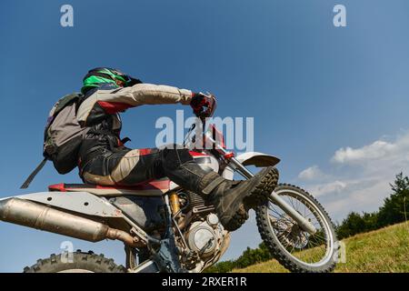 Un pilota professionista di motocross impavido esegue con abilità un'estrema manovrabilità all'indietro attraverso un pericoloso terreno forestale, mostrando una straordinaria esperienza Foto Stock