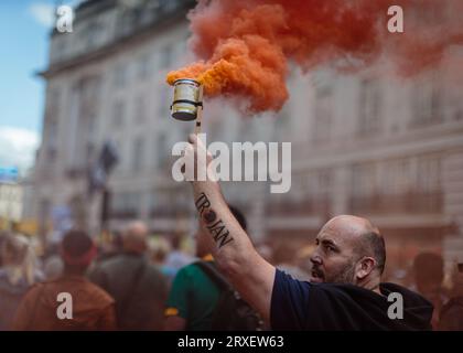 Un manifestante lascia fuori del fumo colorato mentre marciano attraverso Londra protestando contro ULEZ e la sua espansione. Foto Stock