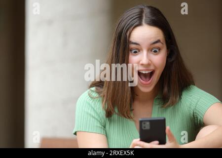 Ritratto frontale di una donna stupita che guarda contenuti sorprendenti al telefono per strada Foto Stock