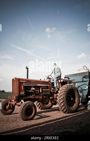 Un uomo si alza sul trattore per avere una visione migliore del campo nella fattoria di famiglia a Keymar, Maryland. Foto Stock