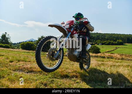 Un pilota professionista di motocross impavido esegue con abilità un'estrema manovrabilità all'indietro attraverso un pericoloso terreno forestale, mostrando una straordinaria esperienza Foto Stock