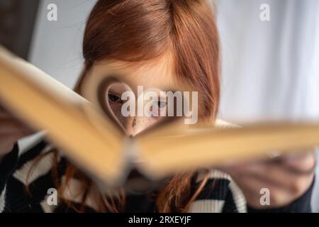 Una ragazza ha un libro in mano. pagine a forma di cuore. Leggere, sapere, imparare Foto Stock