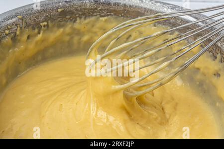 Impasto liquido in un recipiente di ferro con una frusta. Preparare l'impasto per una torta dolce. Foto di alta qualità Foto Stock