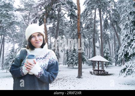 Donna con una tazza di bevanda calda su sfondo innevato invernale. Foto Stock