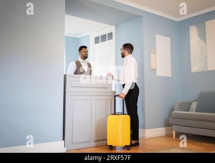 Uomo d'affari del Medio Oriente con valigia che effettua il check-in alla reception dell'hotel Foto Stock