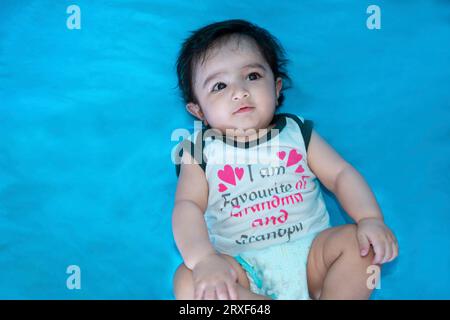 Bambino indiano di sei mesi con pannolino, isolato sul pavimento su sfondo blu, bambino felice con i capelli neri. Foto Stock