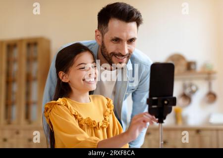 Happy Daughter and Father using smartphone on Tripod at Home Foto Stock