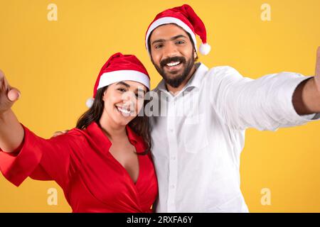 Un uomo arabo millenario sorridente con il cappello di Babbo Natale abbraccia signora, facendo selfie Foto Stock