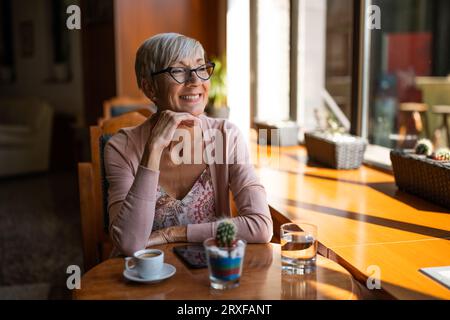 Una donna matura è seduta in una caffetteria e si sta rilassando. Foto Stock