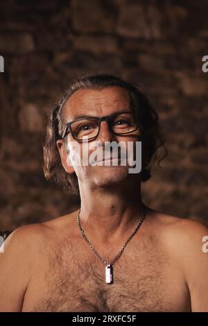 Un uomo più anziano, di circa 60 anni, di nazionalità serba con capelli lunghi che indossa occhiali su sfondo scuro guarda la fotocamera. Artista, creativo Foto Stock