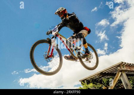 l'atleta di mountainbiker salta giù in volo. sullo sfondo del cielo blu Foto Stock