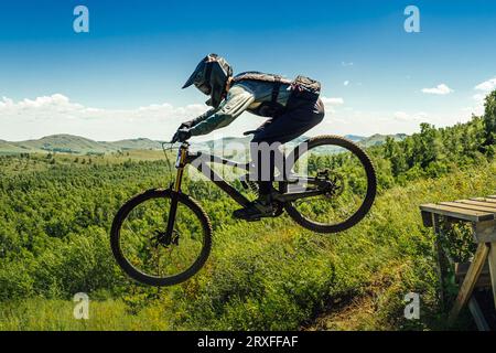 l'atleta di mountainbiker salta giù in volo. sullo sfondo delle montagne nella verde foresta Foto Stock