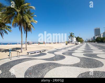 Famosa passeggiata sul lungomare sulla spiaggia di Copacabana e alberi di cocco con cielo blu a Rio de Janeiro in Brasile. Foto Stock