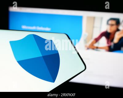 Telefono cellulare con logo del software di sicurezza Microsoft Defender Antivirus sullo schermo davanti al sito Web. Concentrarsi sul centro del display del telefono. Foto Stock