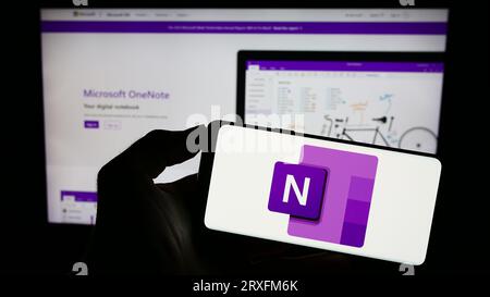Persona che possiede un telefono cellulare con il logo del software per prendere appunti Microsoft OneNote sullo schermo davanti alla pagina Web aziendale. Concentrarsi sul display del telefono. Foto Stock