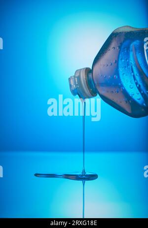 Bottiglia di detergente liquido inclinabile verso il basso con liquido che fuoriesce sulla superficie sottostante. Foto Stock