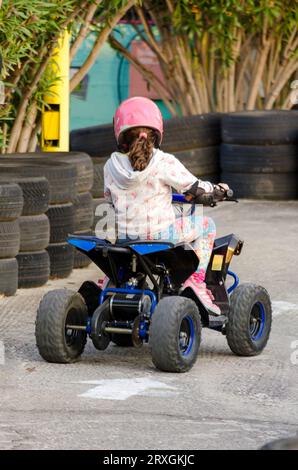 Little Girl guida un quad per motociclette con quattro ruote. Attività all'aperto per bambini su una macchina da corsa elettrica Quad. Il bambino indossa le attrezzature di sicurezza Foto Stock