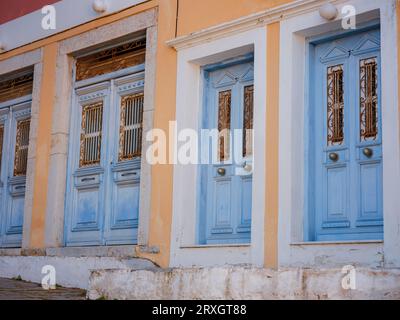 Graziosi dettagli di finestre, porte e balconi di una vecchia casa sull'isola di Simi. Vacanze nelle isole della Grecia da Rodi nel Mar Egeo. Case colorate in stile neoclassico nella baia di Symi. Informazioni generali sui viaggi di vacanza. Foto Stock