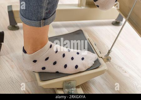 Piedi femmina sul pedale di una macchina da cucire, primo piano del motore Foto Stock