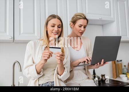 belle sorelle in un elegante stile pastello con carta di credito e computer portatile e un legame familiare Foto Stock