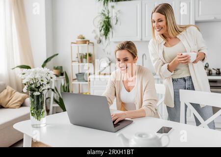 belle sorelle allegri in un bell'abbigliamento che guardano un computer portatile e che tengano una tazza di tè Foto Stock