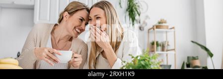 bellissime sorelle dall'aspetto informale che bevono tè e sorridono in cucina, legano, striscione Foto Stock