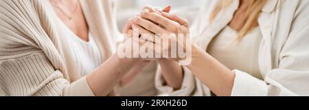 vista ritagliata delle sorelle bionde dall'aspetto gradevole in incantevoli abiti casual che tengono per mano, legano, striscione Foto Stock