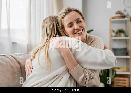due sorelle bionde in un bell'abbigliamento informale abbracciano il divano con gli occhi chiusi, legando la famiglia Foto Stock