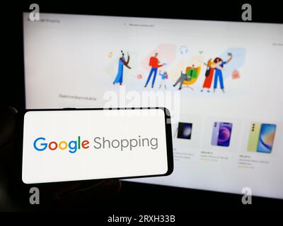Persona che possiede uno smartphone con il logo della piattaforma di ricerca dei prodotti Google Shopping sullo schermo di fronte al sito Web. Concentrarsi sul display del telefono. Foto Stock